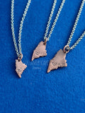 Three sizes of Copper pendants in the shape of the state of Maine with hearts stamped into their lower left sides.  Each pendant is on its own stainless steel chain. Lewiston Strong.